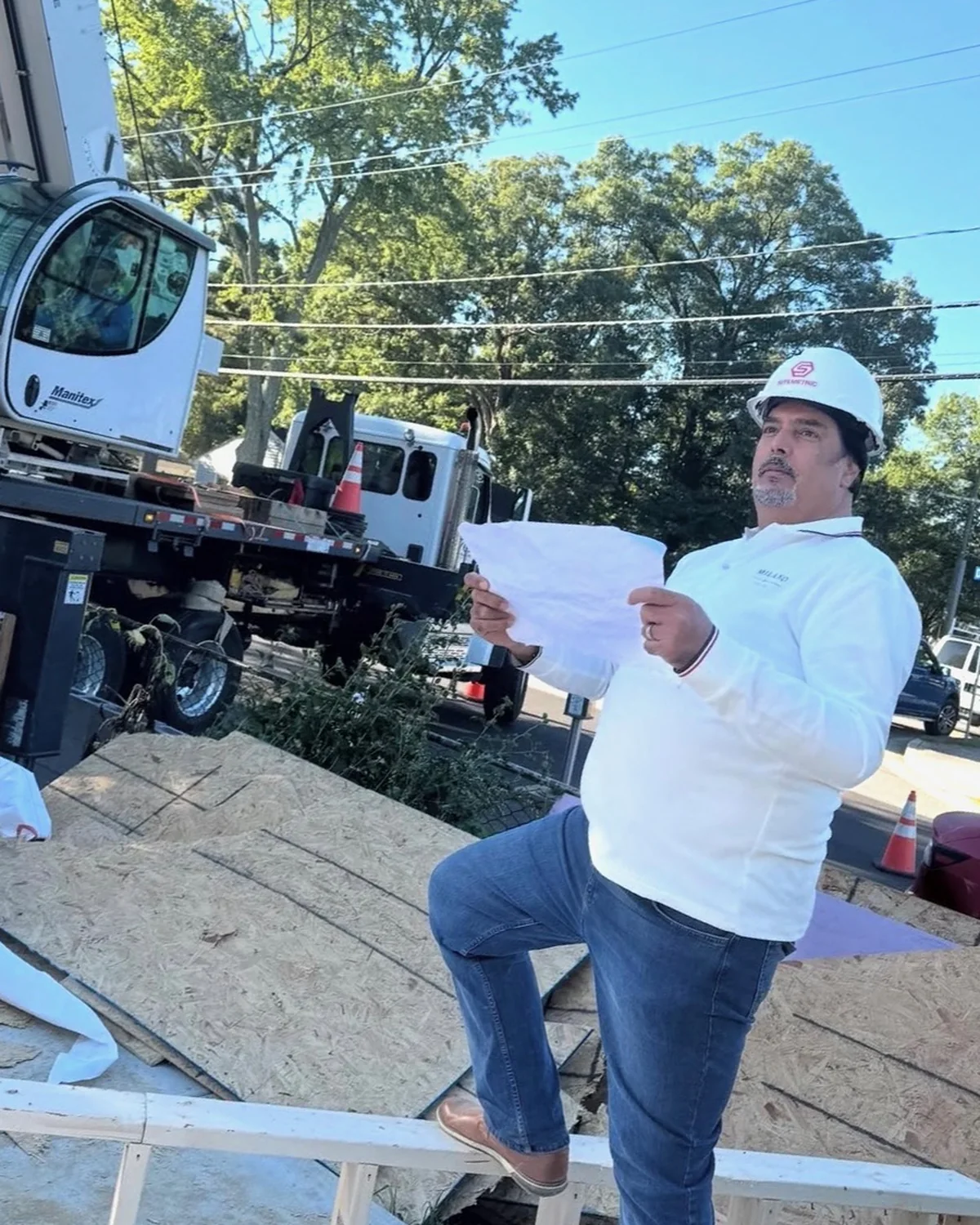 Shawn Waziri on site in a hard hat, reading plans, with a crane and new framing behind him