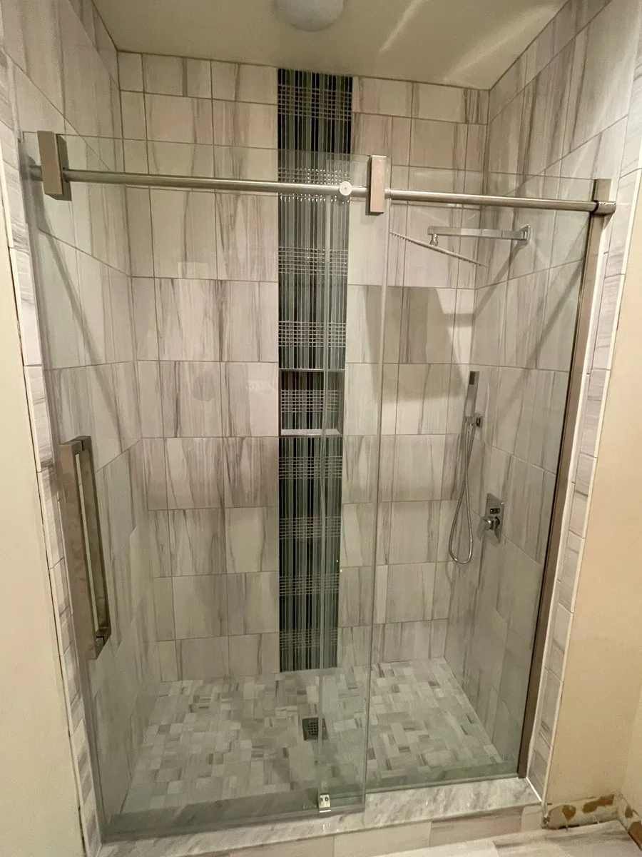 A tiled shower enclosure in marble-look porcelain with a vertical mosaic niche and a frameless glass door.