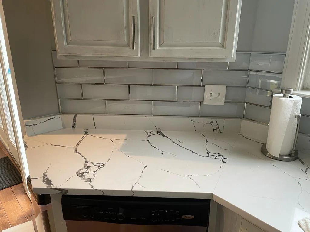 A white quartz countertop with gray veining, continuing up the wall as a matching backsplash.