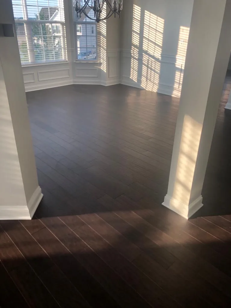An empty open-plan room with dark hardwood flooring and square columns, sunlight falling across the boards.