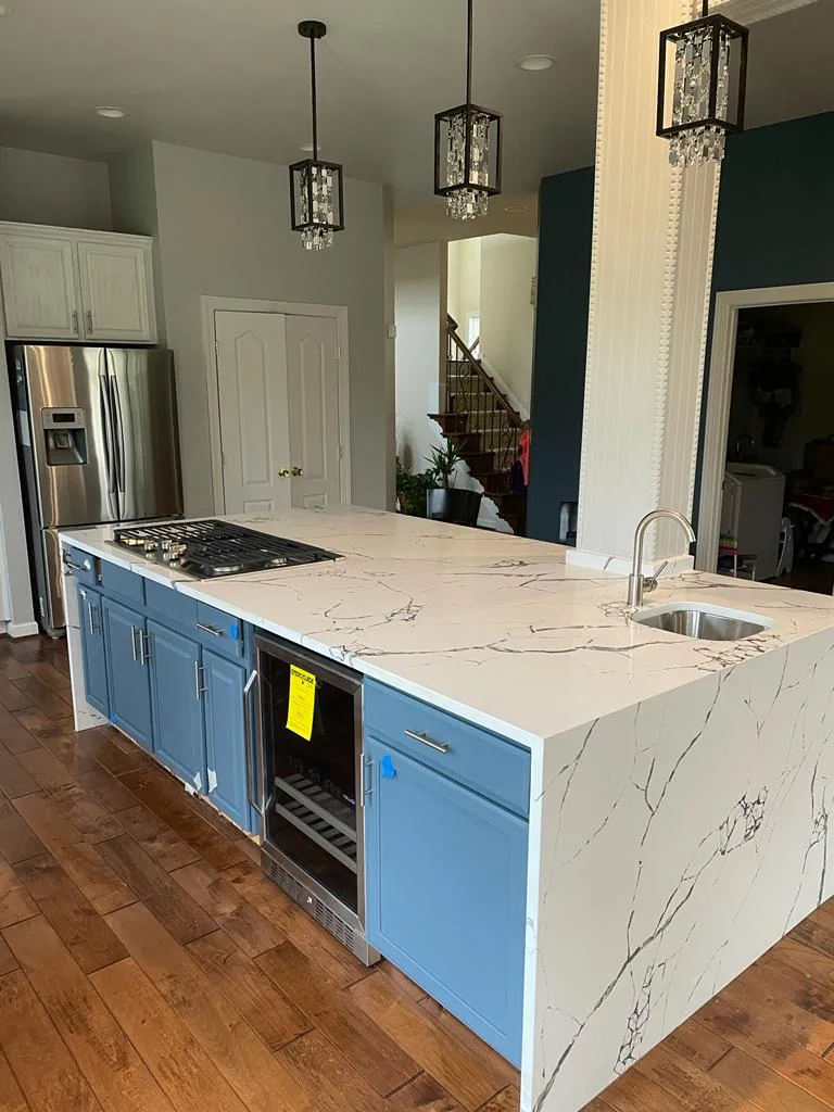 A remodeled kitchen with deep blue base cabinets, a thick white quartz island with gray veining, stainless appliances, and hardwood floors.