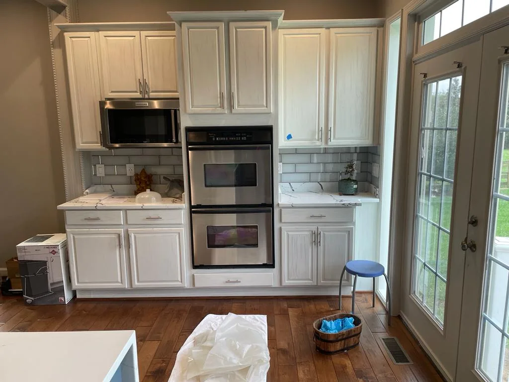 A cream-cabinet kitchen with stainless double ovens installed, protective sheeting still on the floor.