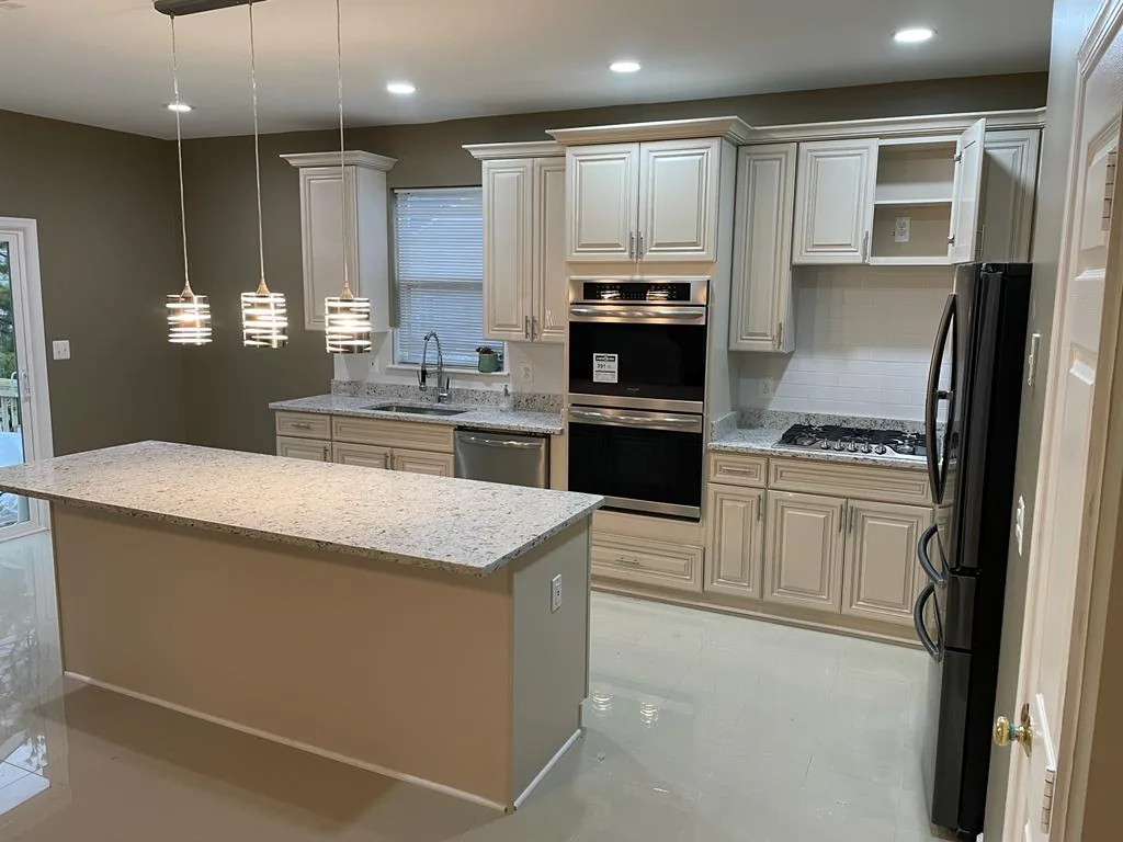 A cream-cabinet kitchen seen across a granite-topped island, with pendant lights above.