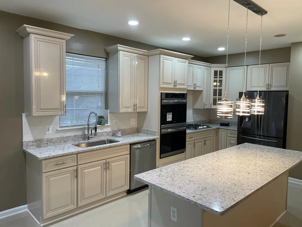 A kitchen with cream raised-panel cabinets, speckled granite counters, wall ovens, and a center island.