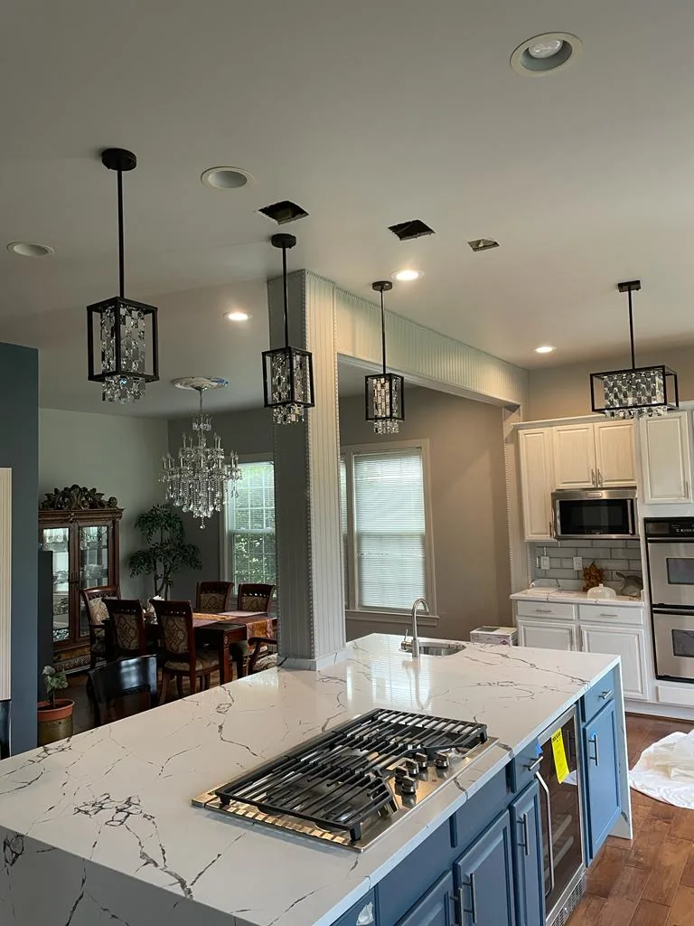 A finished kitchen with three lantern pendant lights above a white quartz island.