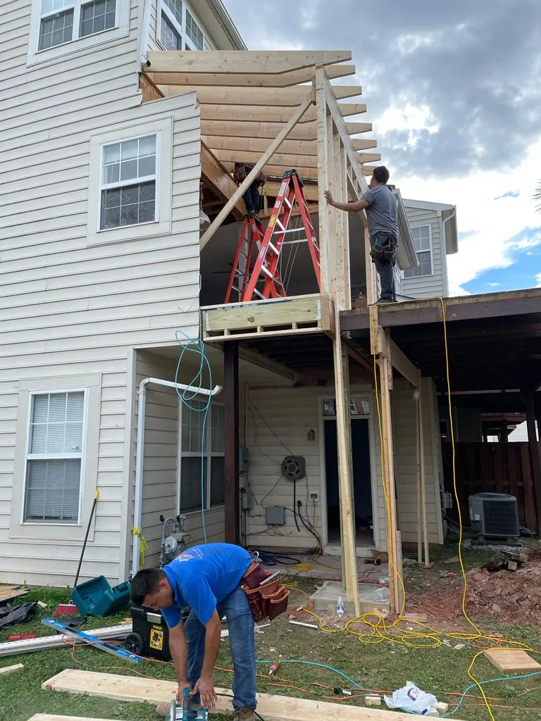 A rear porch addition mid-construction, framing tied into the back of a house, with workers on site.
