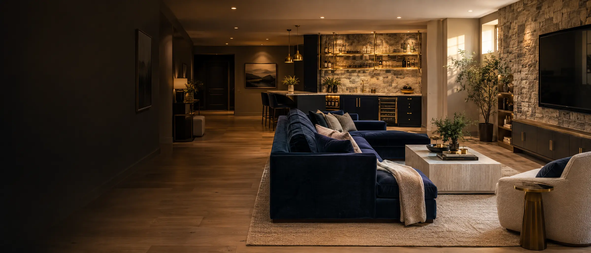 A finished basement lounge with a navy sofa, oak floor, stone wall, and a wet bar