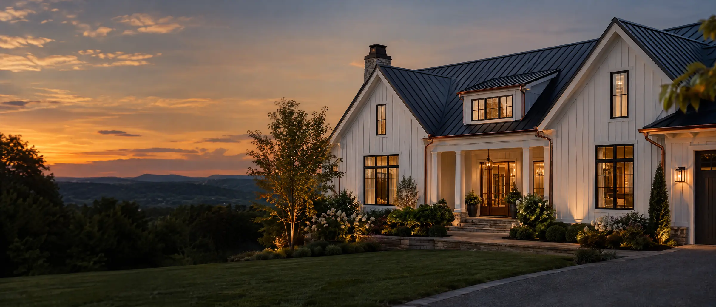 A home with a dark standing-seam metal roof, white board-and-batten siding, and copper gutters at dusk